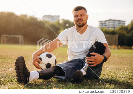 Conception of returning to the sport, sitting. Strong amputee man with prosthesis is with soccer ball on the field 139230829