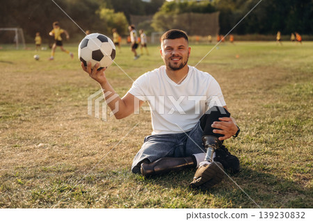 Cheerful facial expression. Strong amputee man with prosthesis is with soccer ball on the field Cheerful facial expression. Strong amputee man with prosthesis is with soccer ball on the field 139230832