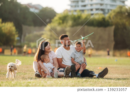 Sitting on the ground, playing with toy plane. Mother, amputee father with prosthesis and kids are on the field 139231057