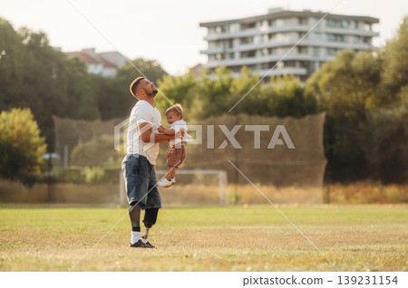 Feeling good, holding kid in hands. The amputee father is with his son on the field Feeling good, holding kid in hands. The amputee father is with his son on the field 139231154
