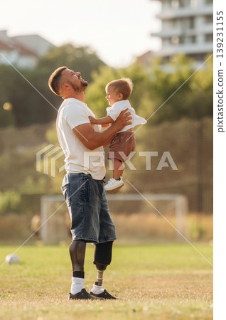 Feeling good, holding kid in hands. The amputee father is with his son on the field Feeling good, holding kid in hands. The amputee father is with his son on the field 139231155
