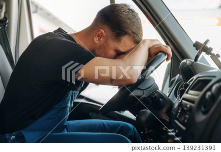 Tired, sleeping on the steering wheel. Inside of the bus with delivery service man in uniform Tired, sleeping on the steering wheel. Inside of the bus with delivery service man in uniform 139231391
