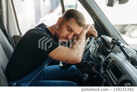Tired, sleeping on the steering wheel. Inside of the bus with delivery service man in uniform Tired, sleeping on the steering wheel. Inside of the bus with delivery service man in uniform 139231392