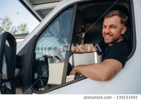 Sitting in a van and smiling. Courier of delivery service company is at work Sitting in a van and smiling. Courier of delivery service company is at work 139231402