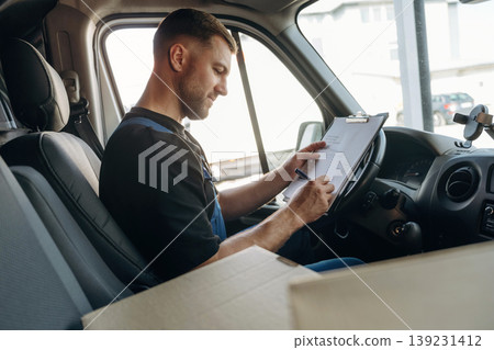 Fills out the document, writes on the invoice. Inside of the bus with delivery service man in uniform Fills out the document, writes on the invoice. Inside of the bus with delivery service man in uniform 139231412