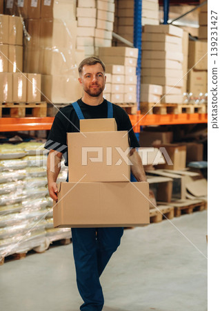 Blue uniform. Holding the box. Man is working in the storage with packages for shipment 139231427
