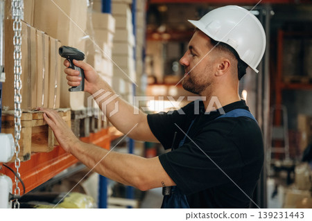 Process of the scan of boxes. Man in uniform is working in the storage with packages for shipment Process of the scan of boxes. Man in uniform is working in the storage with packages for shipment 139231443