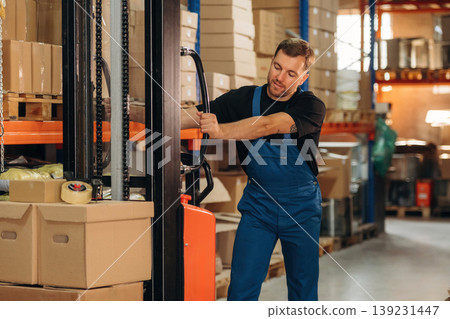Moving stuff by using forklift. Man in uniform is working in the storage with packages for shipment 139231447
