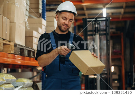 Boxes are getting scanned. Man in uniform is working in the storage with packages for shipment 139231450