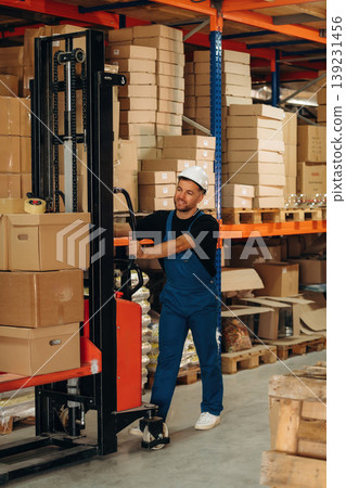 Moving stuff by using forklift. Man in uniform is working in the storage with packages for shipment Moving stuff by using forklift. Man in uniform is working in the storage with packages for shipment 139231456