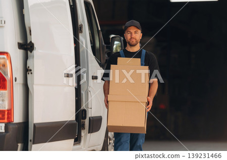 A lot of boxes. Delivery man is by the bus near garage outdoors A lot of boxes. Delivery man is by the bus near garage outdoors 139231466