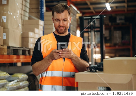 Time for a break, using smartphone. Man in uniform is working in the storage with packages for shipment Time for a break, using smartphone. Man in uniform is working in the storage with packages for shipment 139231489