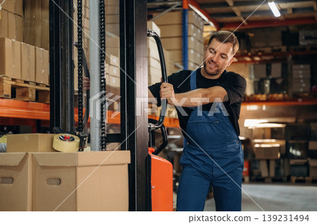 Transporting the boxes by using forklift. Man in uniform is working in the storage with packages for shipment 139231494
