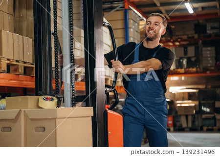 Transporting the boxes by using forklift. Man in uniform is working in the storage with packages for shipment 139231496