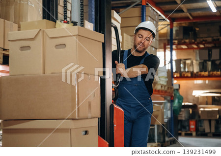 Preparing boxes for shipment by moving them by forklift. Man in uniform is working in the storage 139231499
