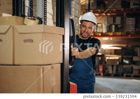 Preparing boxes for shipment by moving them by forklift. Man in uniform is working in the storage Preparing boxes for shipment by moving them by forklift. Man in uniform is working in the storage 139231504