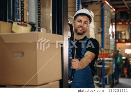 Forklift machine, using machinery to move stuff. Man in uniform is working in the storage with packages for shipment Forklift machine, using machinery to move stuff. Man in uniform is working in the storage with packages for shipment 139231511
