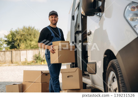 Male courier is near the van, holding the packages Male courier is near the van, holding the packages 139231526