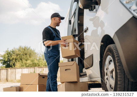 Male courier is near the van, holding the packages Male courier is near the van, holding the packages 139231527