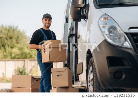Male courier is near the van, holding the packages Male courier is near the van, holding the packages 139231530
