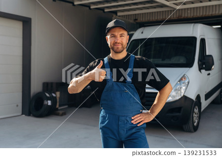 Thumb up, positive facial expression. Delivery man is by the bus near garage outdoors Thumb up, positive facial expression. Delivery man is by the bus near garage outdoors 139231533