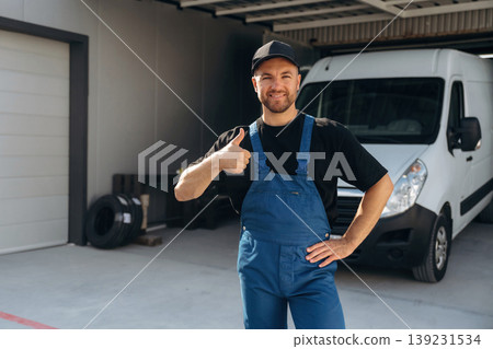 Thumb up, positive facial expression. Delivery man is by the bus near garage outdoors Thumb up, positive facial expression. Delivery man is by the bus near garage outdoors 139231534