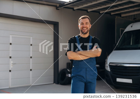 Arms crossed, standing. Delivery man is by the bus near garage outdoors Arms crossed, standing. Delivery man is by the bus near garage outdoors 139231536
