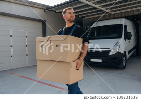 The boxes are in hands. Delivery man is by the bus near garage outdoors 139231539