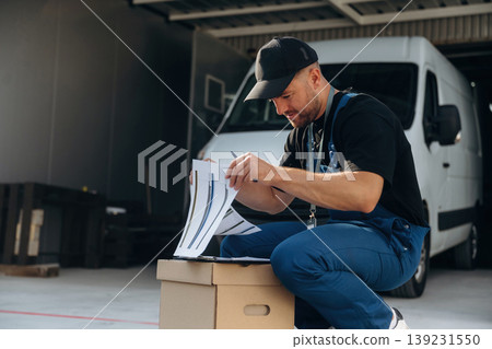 Data in the notepad, holding box. Delivery man is by the bus near garage outdoors 139231550