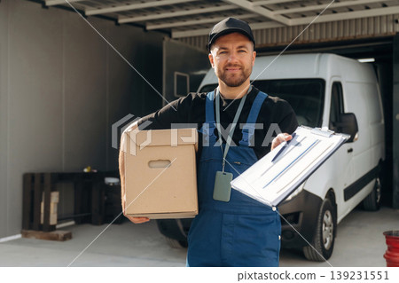 Data in the notepad, holding box. Delivery man is by the bus near garage outdoors 139231551