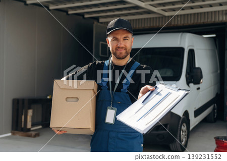 Data in the notepad, holding box. Delivery man is by the bus near garage outdoors 139231552