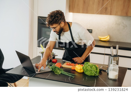 Taking online lessons, using laptop. Handsome man is preparing food on the kitchen 139231824