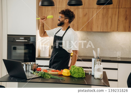 Taking online lessons, using laptop. Handsome man is preparing food on the kitchen Taking online lessons, using laptop. Handsome man is preparing food on the kitchen 139231826