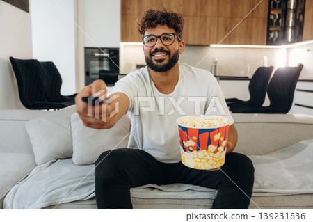 Bucket of popcorn, watching the movie. Man is in the modern domestic room at home Bucket of popcorn, watching the movie. Man is in the modern domestic room at home 139231836