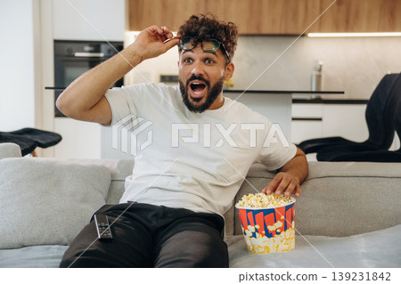 Watching a movie, with popcorn. Man is in the modern domestic room at home Watching a movie, with popcorn. Man is in the modern domestic room at home 139231842