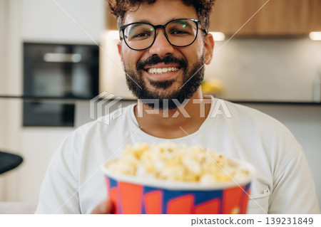 Delicious popcorn in a bucket. Man is in the modern domestic room at home Delicious popcorn in a bucket. Man is in the modern domestic room at home 139231849