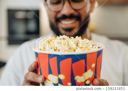 Delicious popcorn in a bucket. Man is in the modern domestic room at home Delicious popcorn in a bucket. Man is in the modern domestic room at home 139231851
