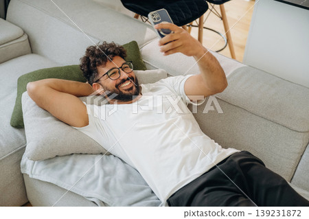 Data in the smartphone, holding it in hand. Man is lying down on the sofa at home, relaxing, feeling good 139231872