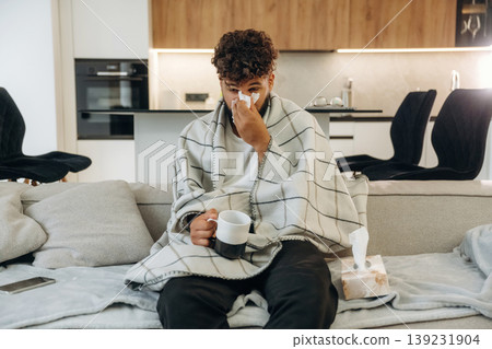 Warm tea in the cup. Sick man is on the sofa at home, with towel, feeling bad 139231904