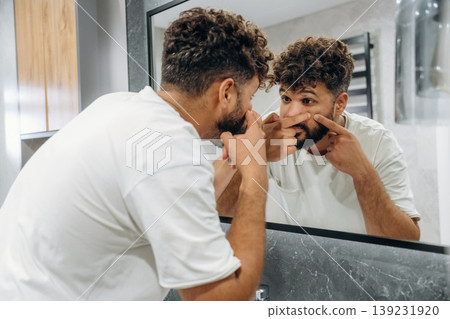 Squeezes pimples, pop it. Guy is in the bathroom, taking care of his appearance Squeezes pimples, pop it. Guy is in the bathroom, taking care of his appearance 139231920