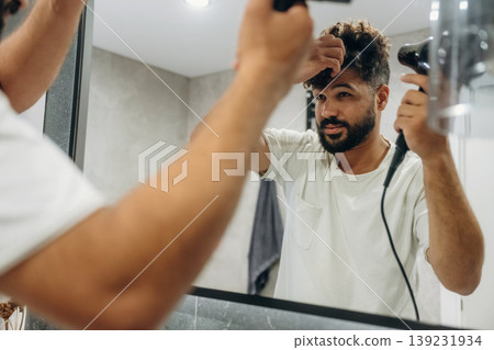 Using hair dryer. Guy is in the bathroom, taking care of his appearance 139231934