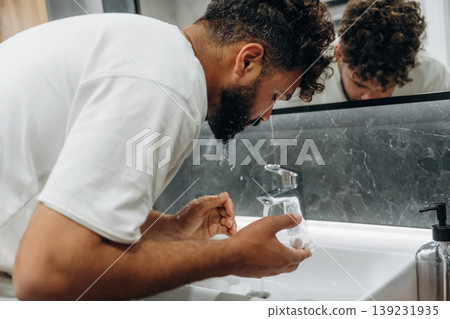 Washes face. Guy is in the bathroom, taking care of his appearance 139231935