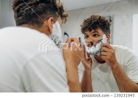Shaves the beard. Guy is in the bathroom, taking care of his appearance Shaves the beard. Guy is in the bathroom, taking care of his appearance 139231945