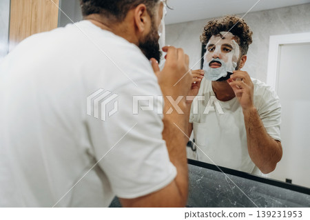 Put on a face mask, conception of beauty. Guy is in the bathroom, taking care of his appearance Put on a face mask, conception of beauty. Guy is in the bathroom, taking care of his appearance 139231953