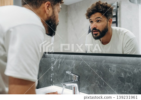 Washes face. Guy is in the bathroom, taking care of his appearance 139231961
