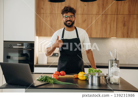 Standing and smiling. Handsome man is preparing food on the kitchen Standing and smiling. Handsome man is preparing food on the kitchen 139231986