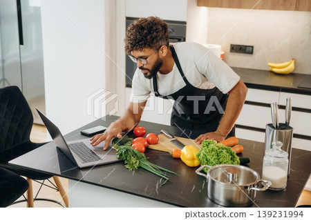 Laptop is on the table. Handsome man is preparing food on the kitchen 139231994