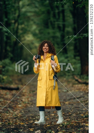 Photographer is with camera. Young woman enjoying nature in the forest under the rain Photographer is with camera. Young woman enjoying nature in the forest under the rain 139232150