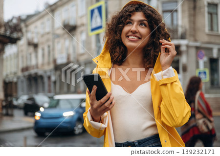 Texting by using smartphone. Happy young woman in the city during the rain 139232171