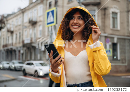Texting by using smartphone. Happy young woman in the city during the rain 139232172